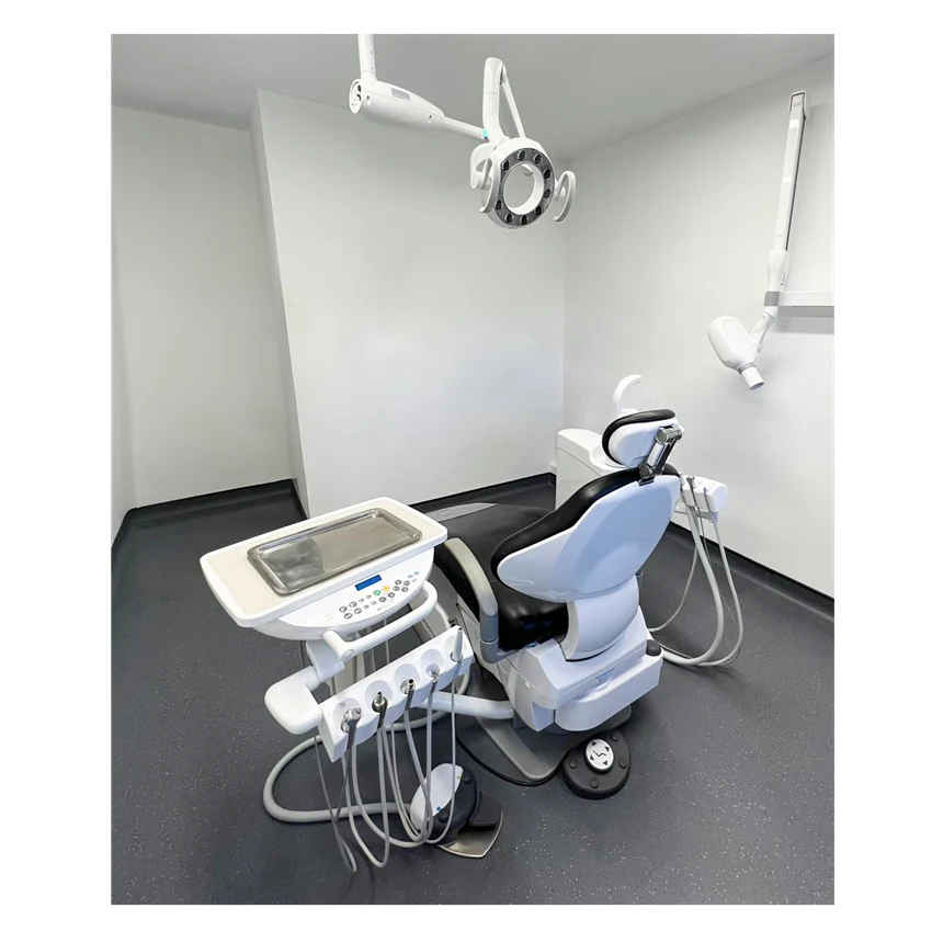 A Belmont dental chair with an attached treatment arm, control console, and dental handpieces, shown in a clean dental office room with white walls and a dark floor.