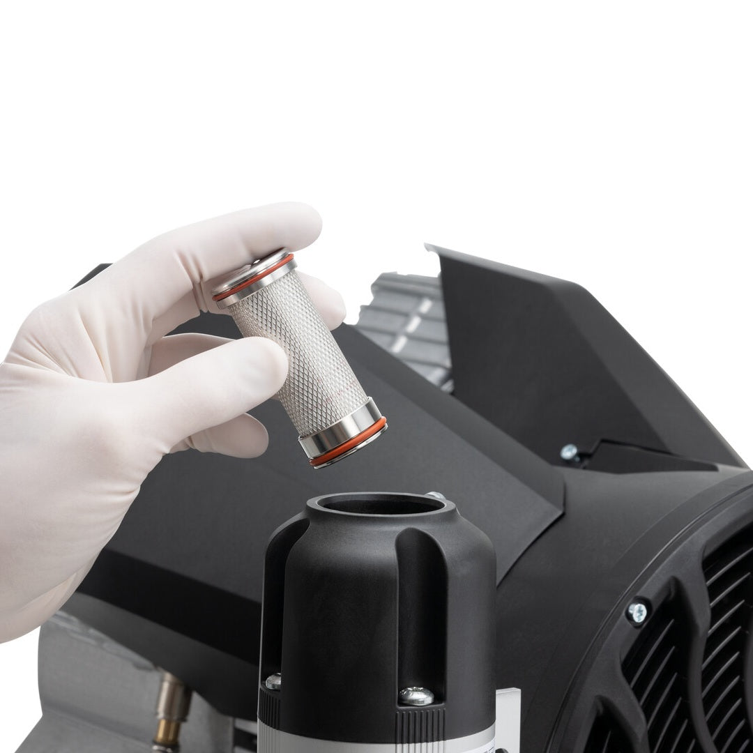 A gloved hand holding a small replacement air filter that is being placed inside the top of a Durr air compressor.